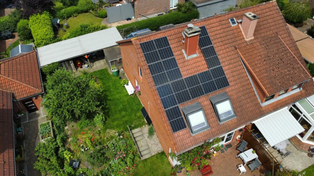 Luftaufnahme eines Wohnhauses, dem wahren Helden des nachhaltigen Lebens, mit Photovoltaik auf dem Dach, einem grünen Hinterhof und Nachbarhäusern in der Umgebung. Das Haus verfügt über Oberlichter und einen Schornstein.